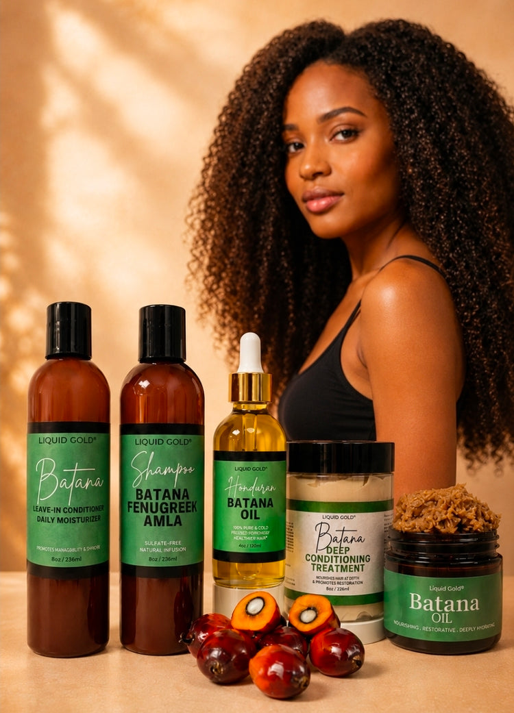 A group of Liquid Gold haircare products arranged in front of a model with long, curly black hair. The products include Batana hair conditioner, Batana Fenugreek Amla shampoo, Batana Oil, a Deep Conditioning Treatment jar, and a Batana Oil jar, with fresh green palm leaves in the foreground on a warm beige background.
