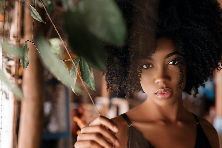 Woman with an afro holding a leaf in a blurred indoor setting